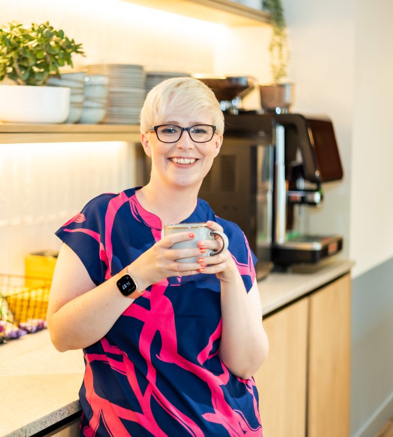 Jenny in a kitchen holding a mug, smiling