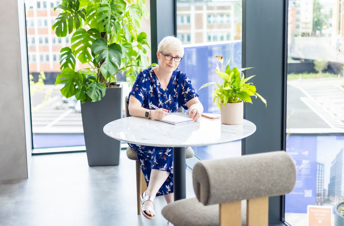 Jenny writing at a table surrounded by plants