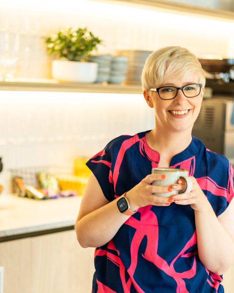 Jenny Lucas smiling, holding a mug in a kitchen